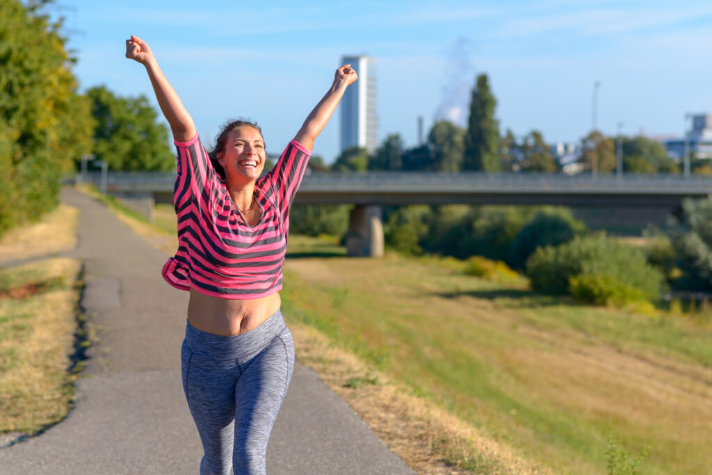 Happy fit young woman cheering and celebrating as she walks along a river after working out jogging. 5 Habits for Intuitive Eating